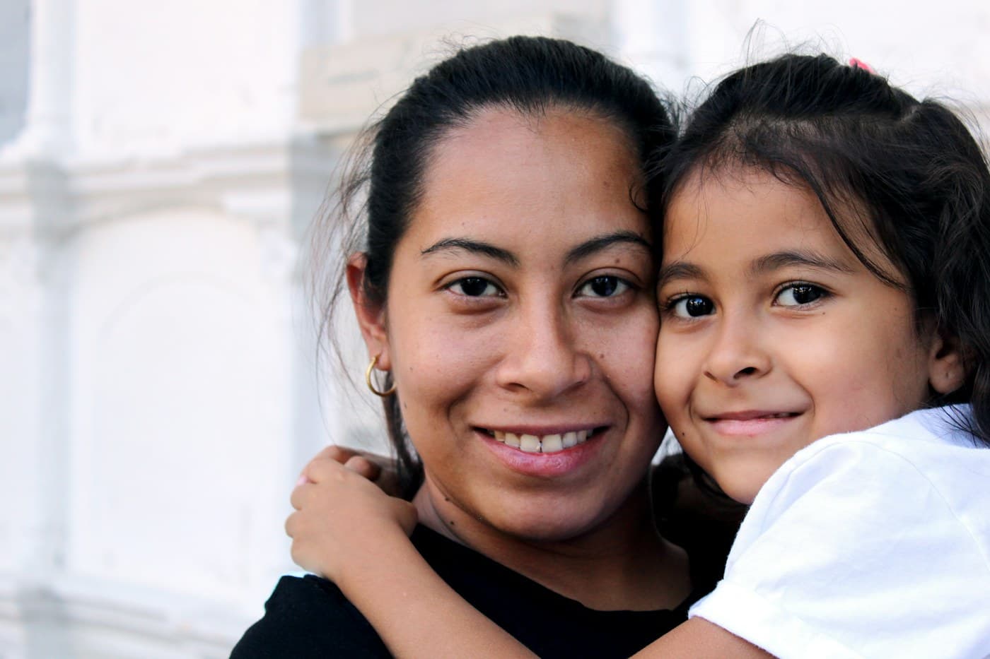 A carer and a girl hugging cheek to cheek, both smiling