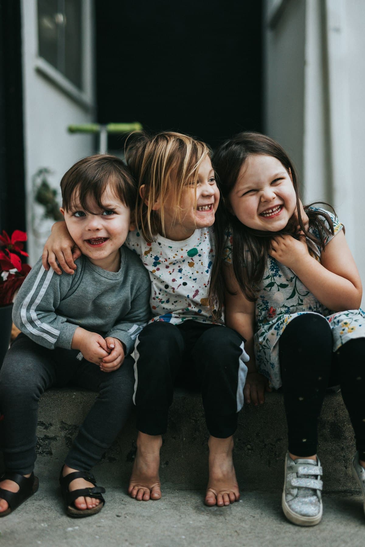 Three children sitting close together on a doorstep, laughing